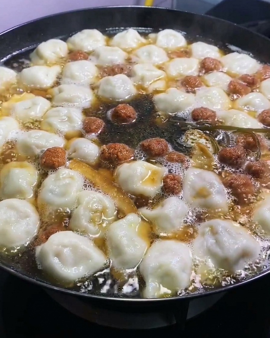 Dark soy sauce being added to a large pot of simmering dumplings and ingredients, adding rich color.