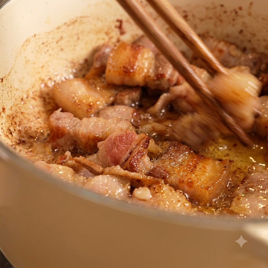 Chopsticks stirring browned meat pieces frying in oil inside a white pot.