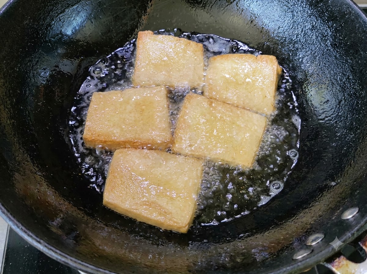 Golden tofu pieces frying in a wok of bubbling oil.