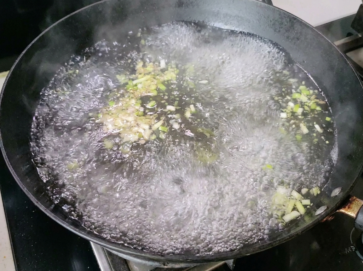 Boiling water with scallions and ginger producing steam in the wok.