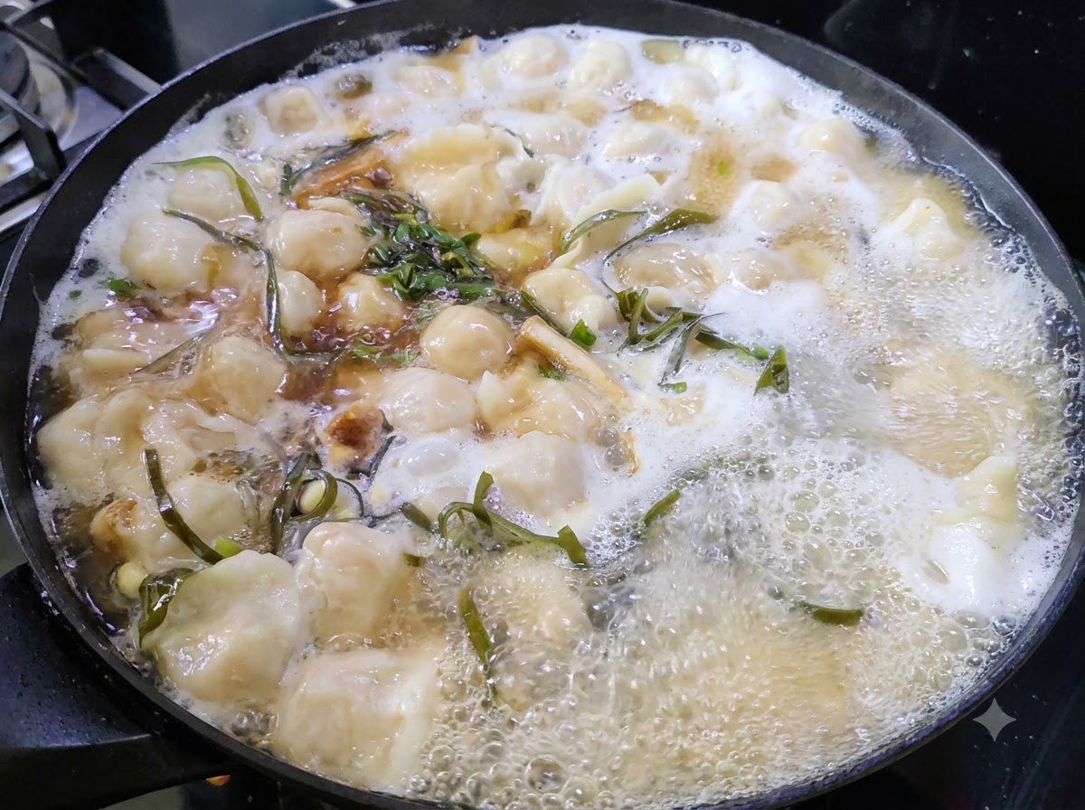 Chopped green herbs floating on the surface of a simmering pot of dumpling soup.