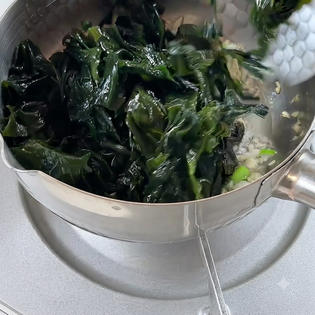 Rehydrated seaweed being added to the pot containing fried garlic and onions.