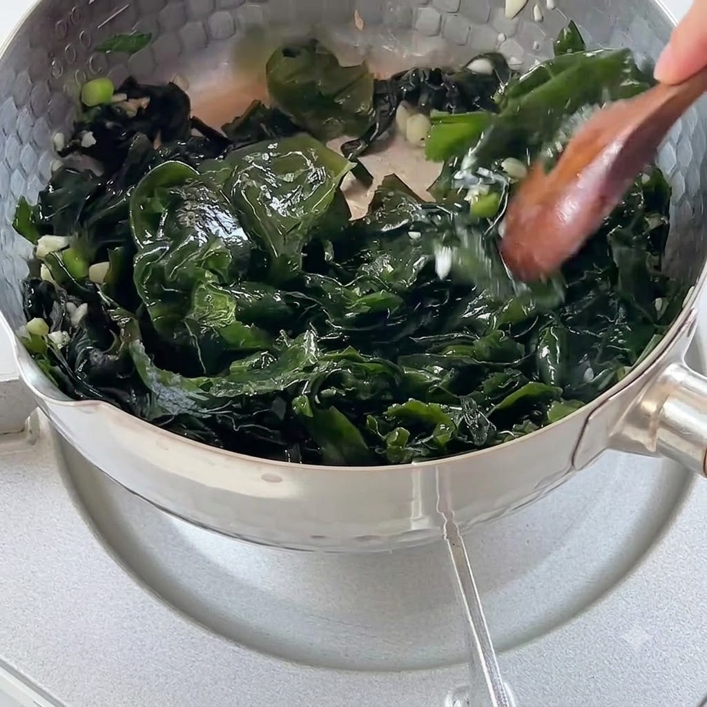 Boiling water being poured into a pot filled with sautéed seaweed and aromatics.