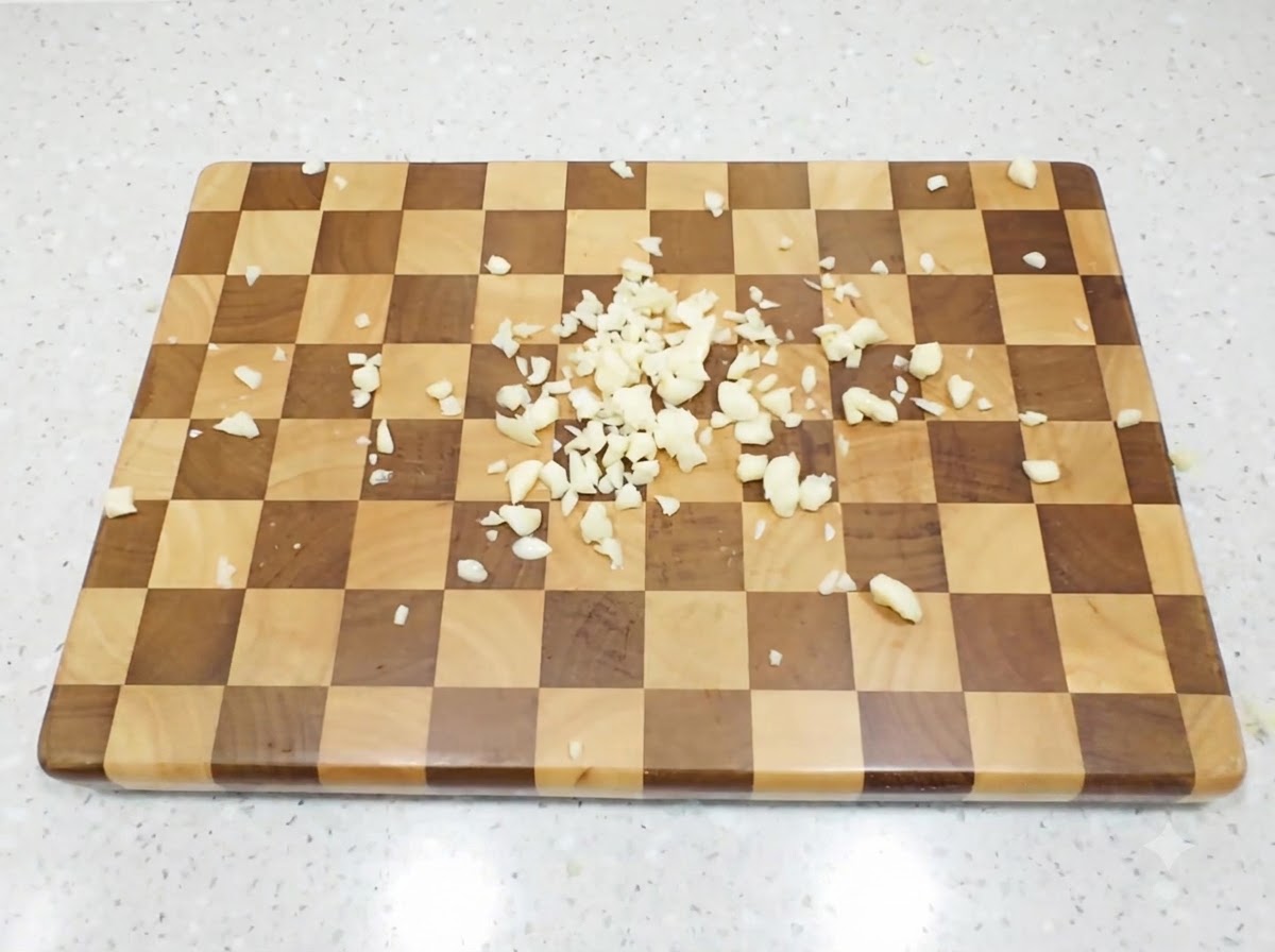 Finely diced garlic cloves scattered across a checkered wooden cutting board.