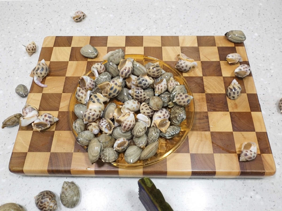 A plate full of raw spotted sea snails resting on a wooden cutting board.