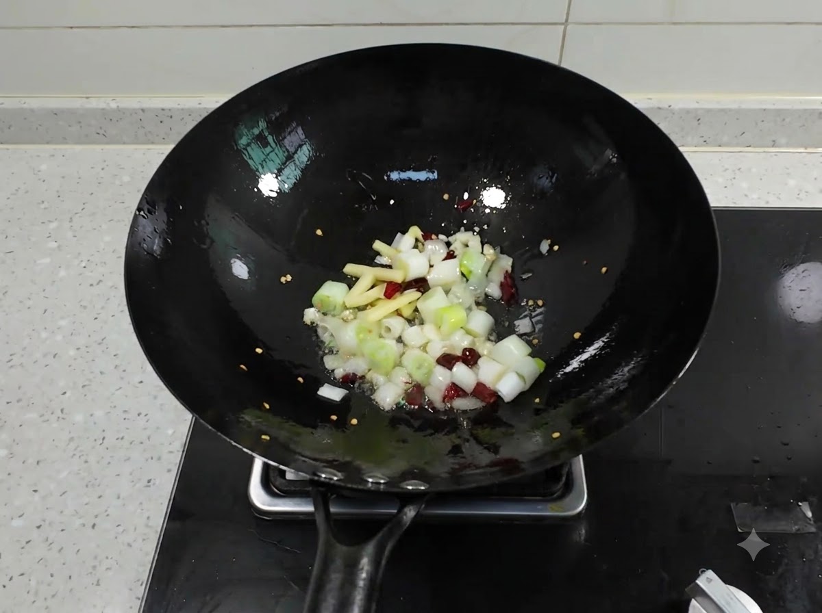 Chopped scallions, ginger, garlic, and dried chilies sizzling in a black wok with hot oil.