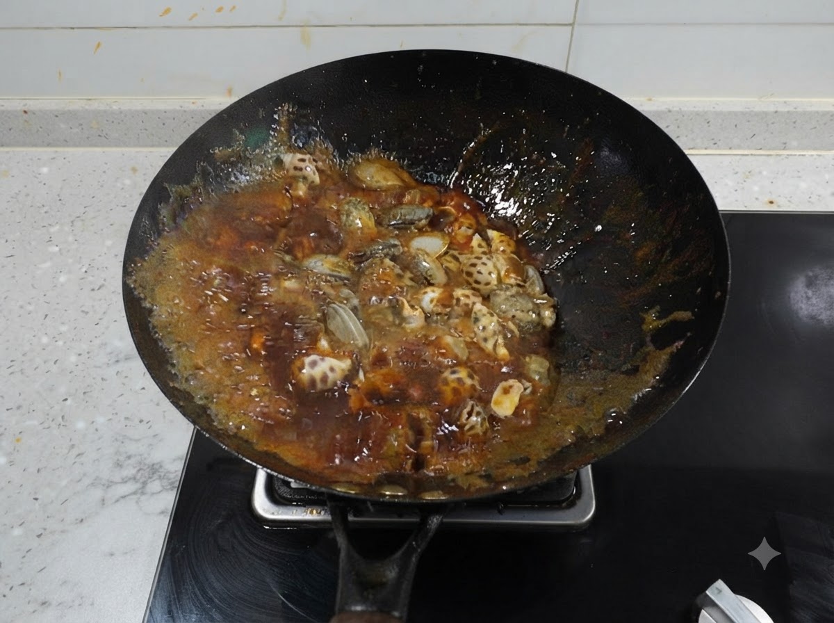 Sea snails and baby octopus simmering in a dark, vigorously bubbling red spicy broth inside a black wok.