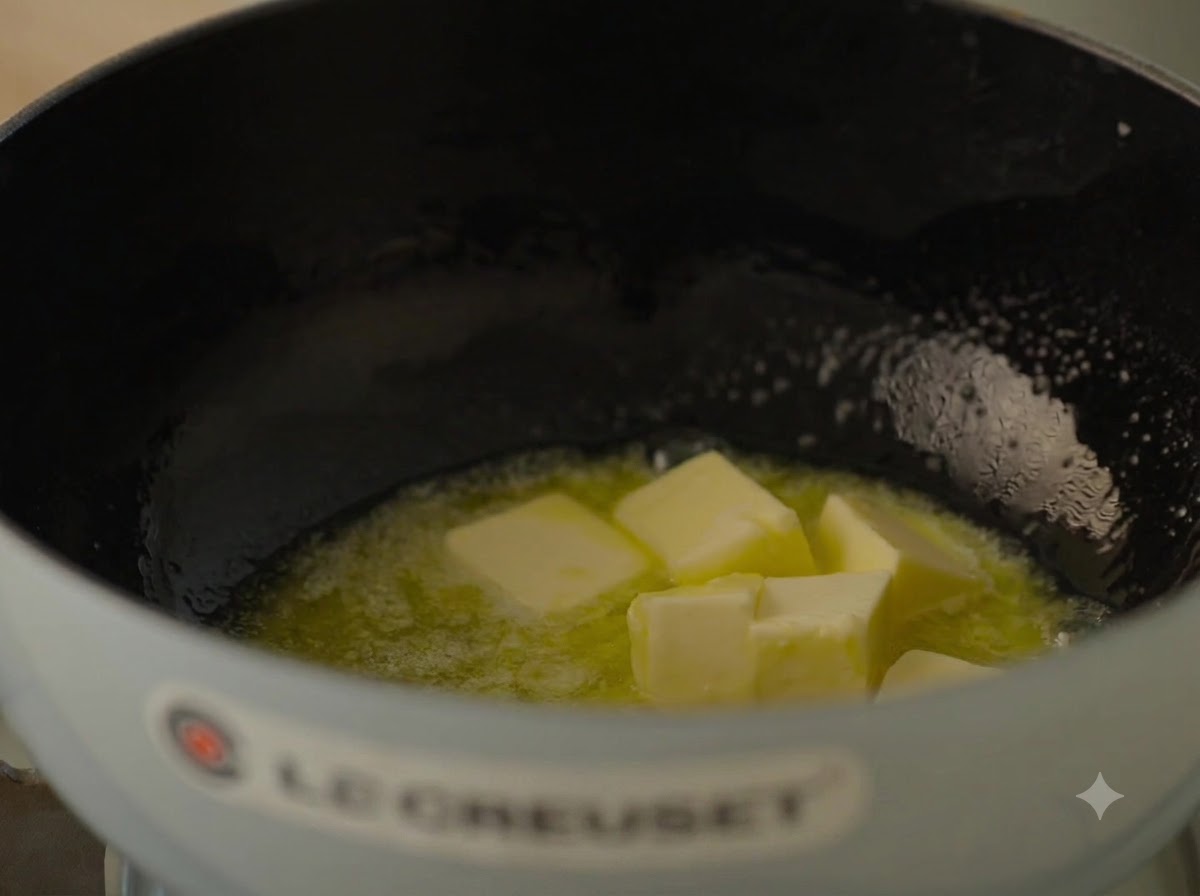 Large chunks of unsalted butter melting and bubbling in a light blue cast-iron pot.