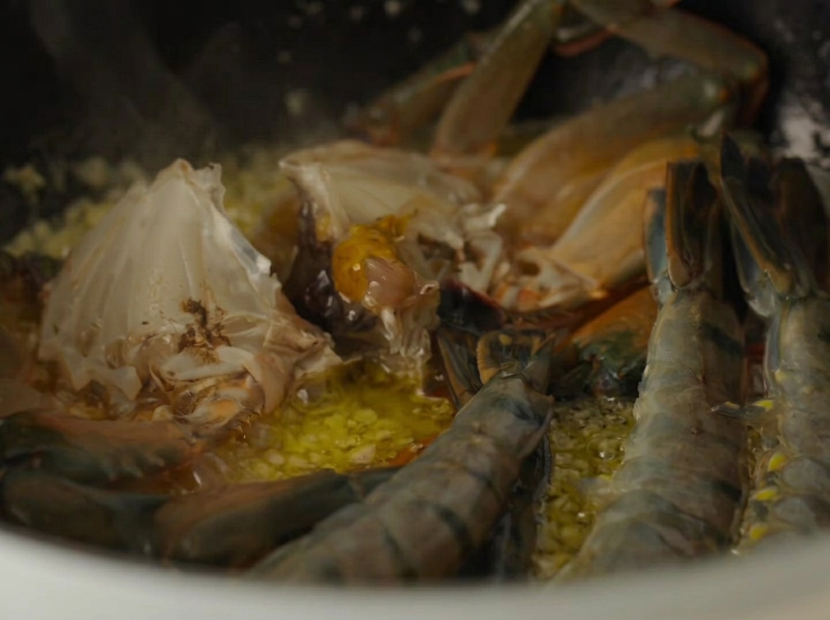 Raw crab parts and raw shrimp cooking inside a pot with garlic butter.