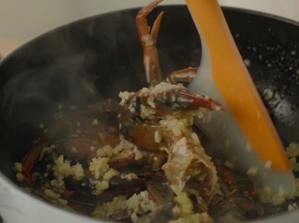 A silicone spatula stirring crab and shrimp inside a steaming pot.