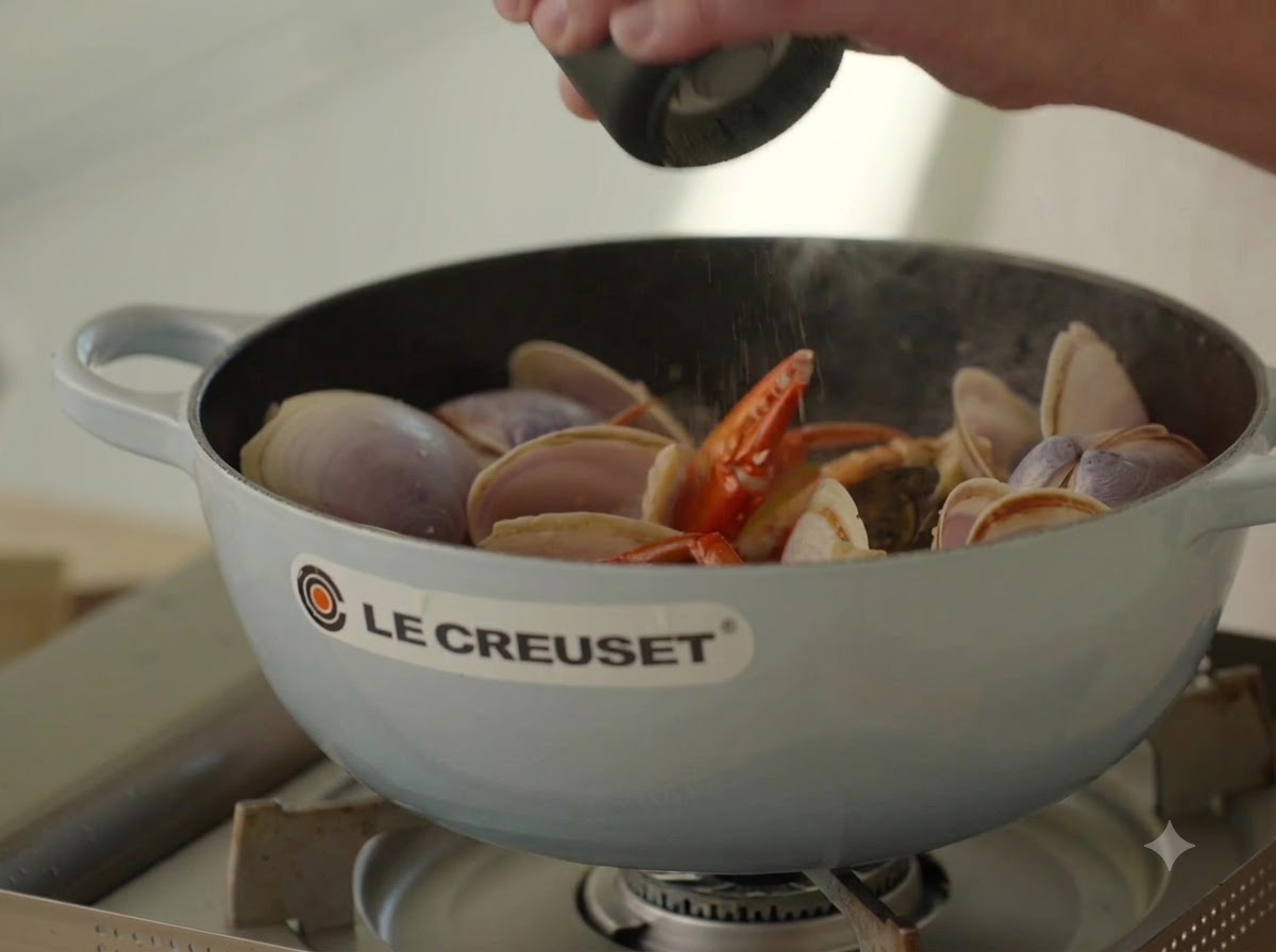 Fresh black pepper being ground over bubbling seafood broth in a pot.
