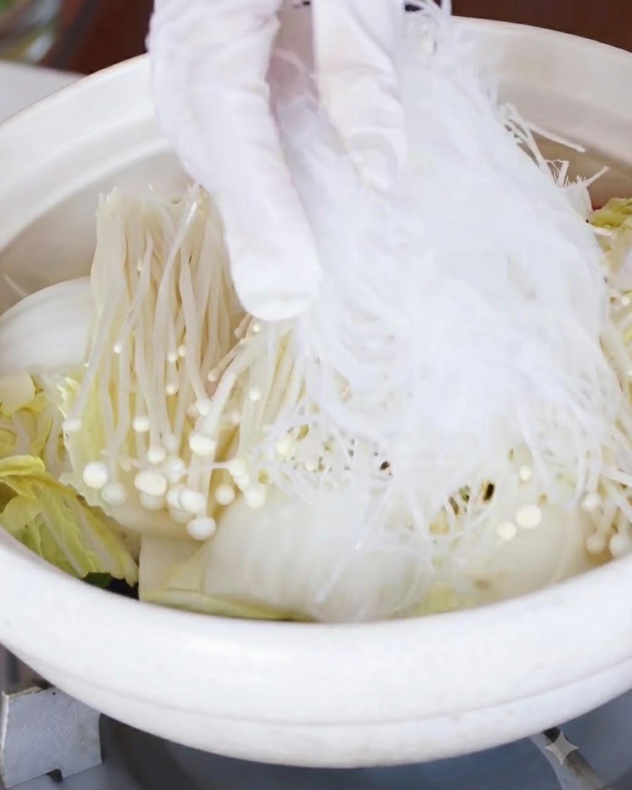 Soaked glass noodles being placed over the layer of enoki mushrooms and cabbage.