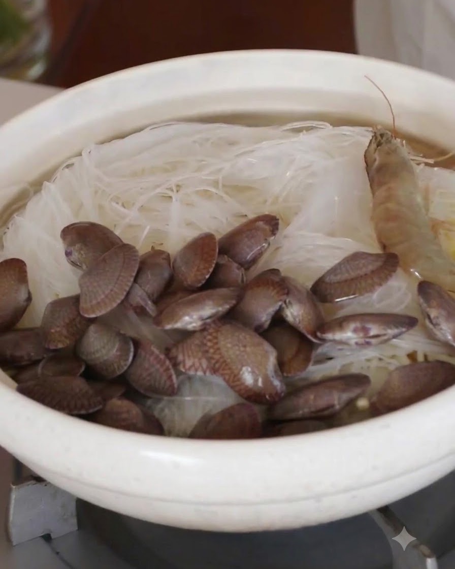Whole raw shrimp and fresh clams arranged in a circle over the glass noodles.