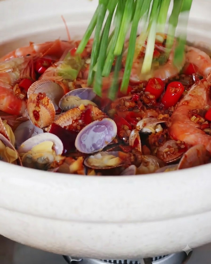 A handful of fresh green onions being sprinkled over a bubbling seafood and noodle pot.