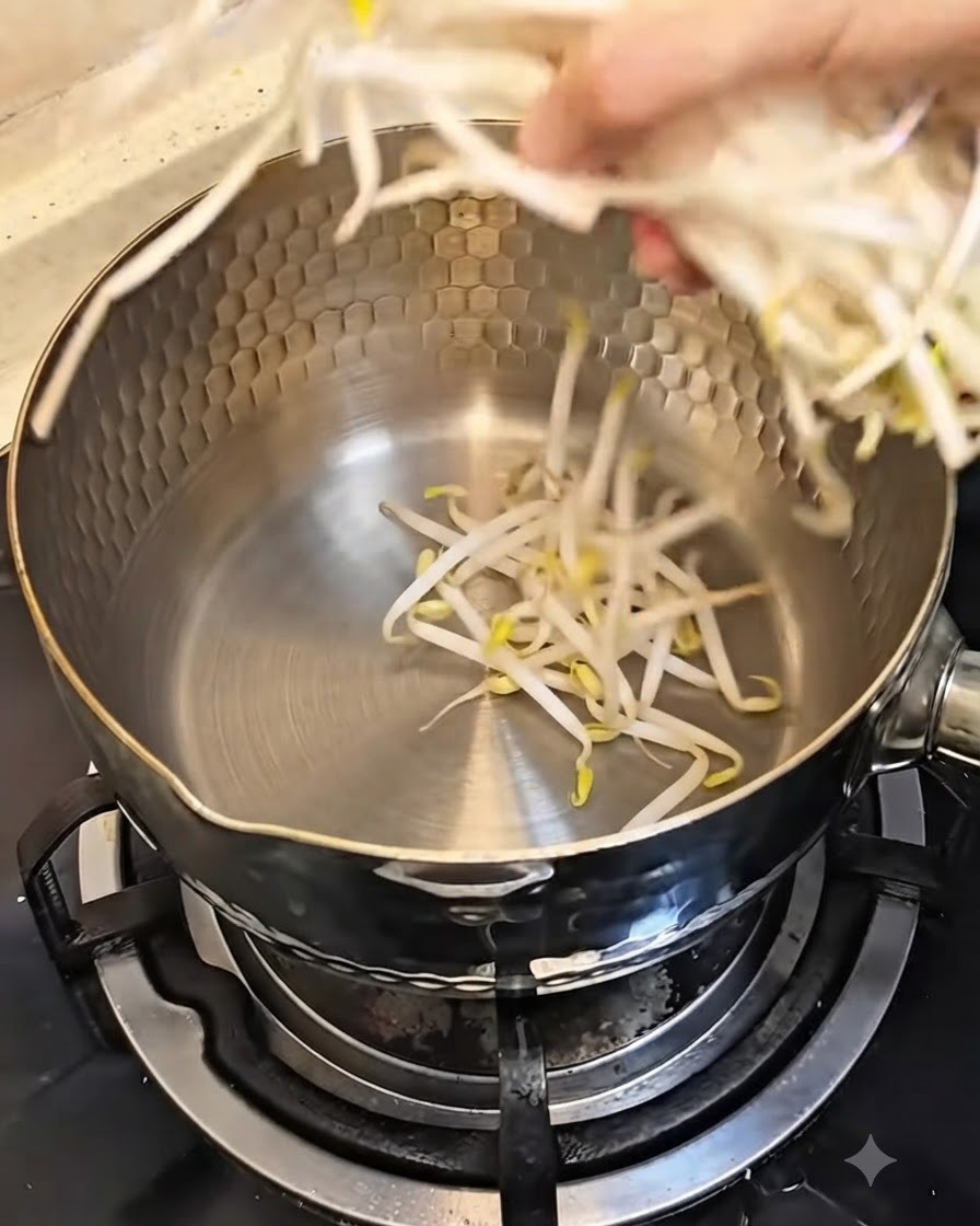 A hand placing a handful of fresh bean sprouts into a clean metal pot.