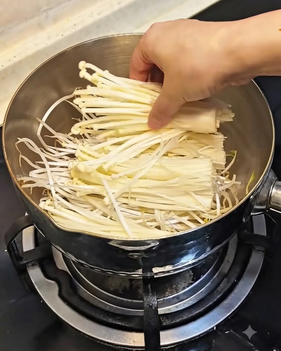 A hand placing a bundle of fresh white enoki mushrooms over the bean sprouts in the pot.