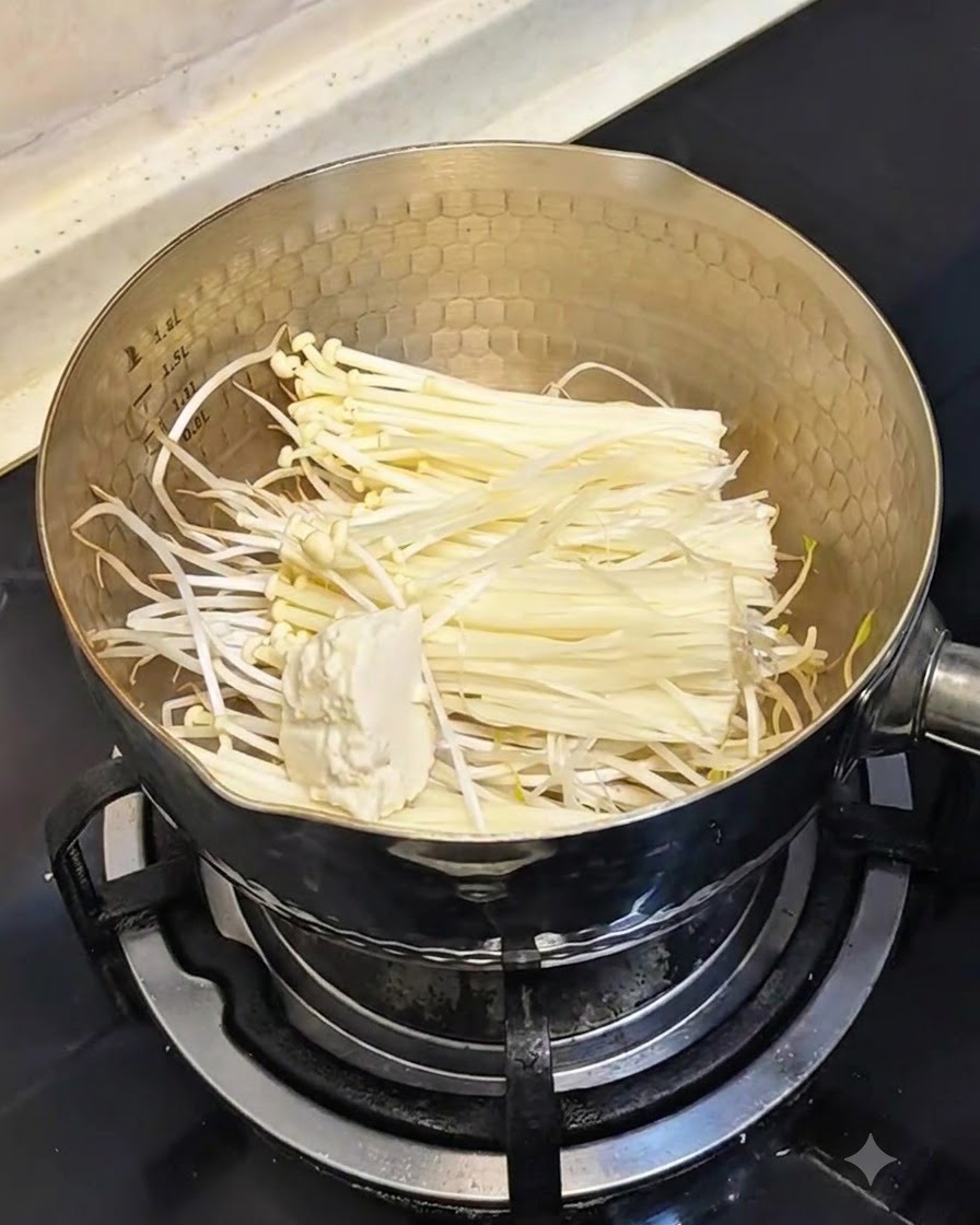 A spoonful of soft silken tofu being added into the pot containing bean sprouts and mushrooms.