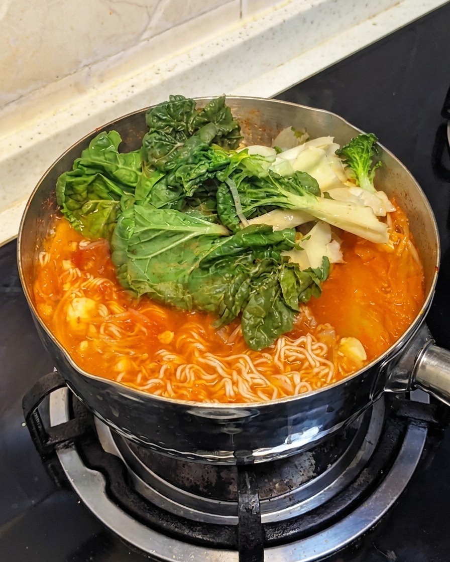 Fresh leafy green vegetables being added on top of the boiling ingredients in the pot.