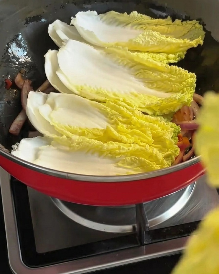 Fresh napa cabbage leaves being layered over the stir-fried onion and kimchi mixture.