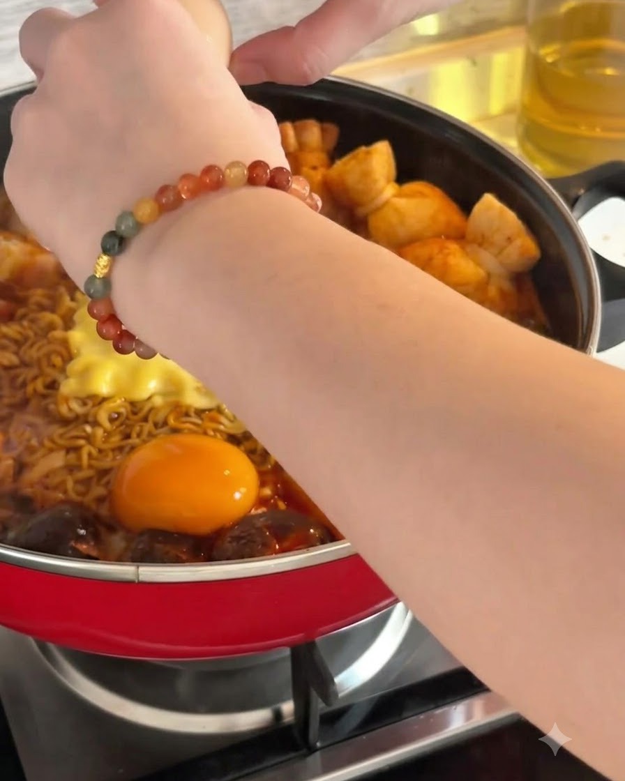 A raw egg being cracked into the hot broth alongside noodles and cheese.