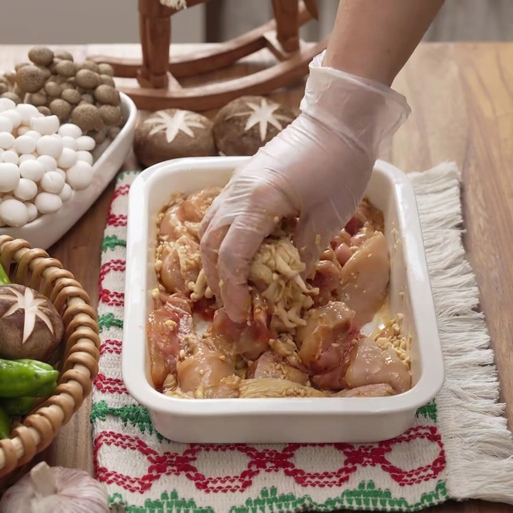 A gloved hand mixing and massaging marinade into chicken pieces inside a white dish.