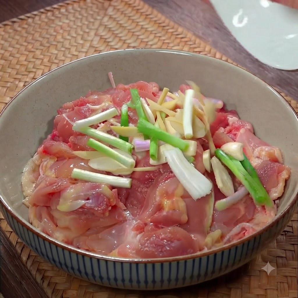 Raw chicken pieces in a ceramic bowl topped with sliced scallions, ginger juliennes, and garlic pieces.