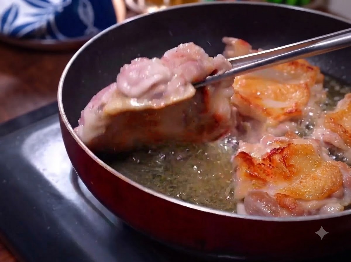 Chicken thighs frying in a skillet with golden-brown skin visible as tongs flip them.