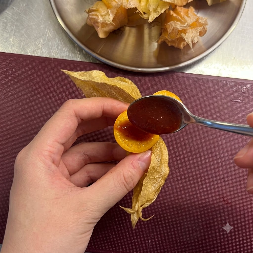 A small spoon adding a dollop of red chili sauce into the hollow center of a sliced cape gooseberry.