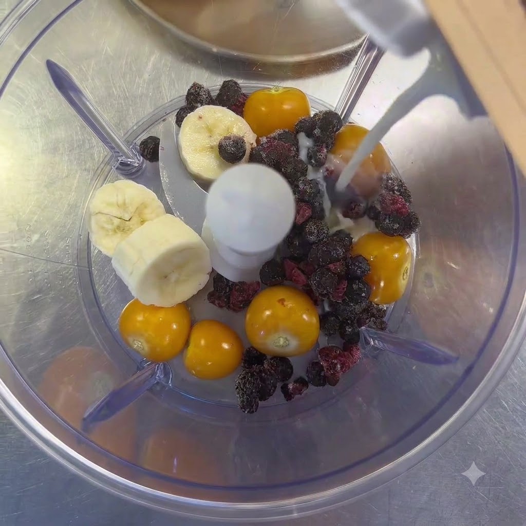 Milk being poured from a carton into a blender filled with cape gooseberries, banana slices, and mixed berries.
