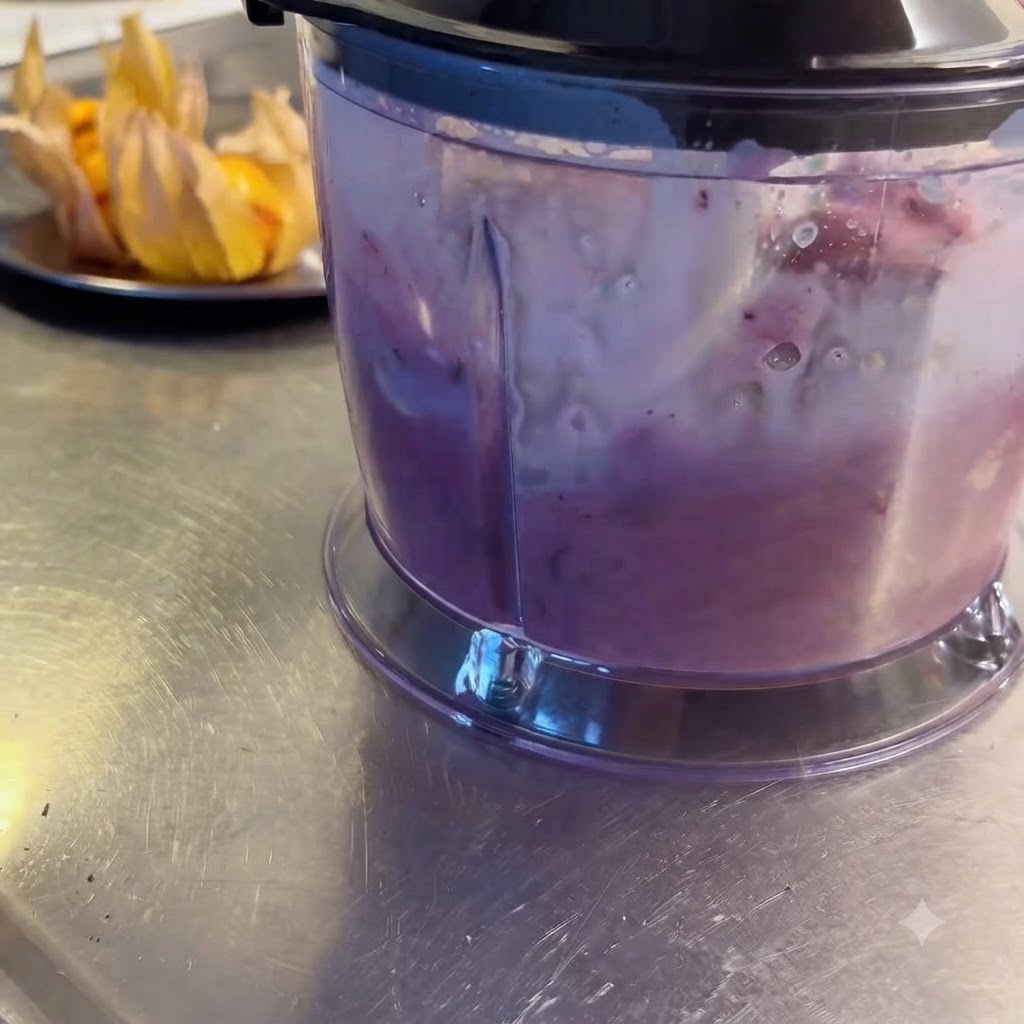 A blender actively processing mixed berries, fruits, and milk into a smooth purple shake.