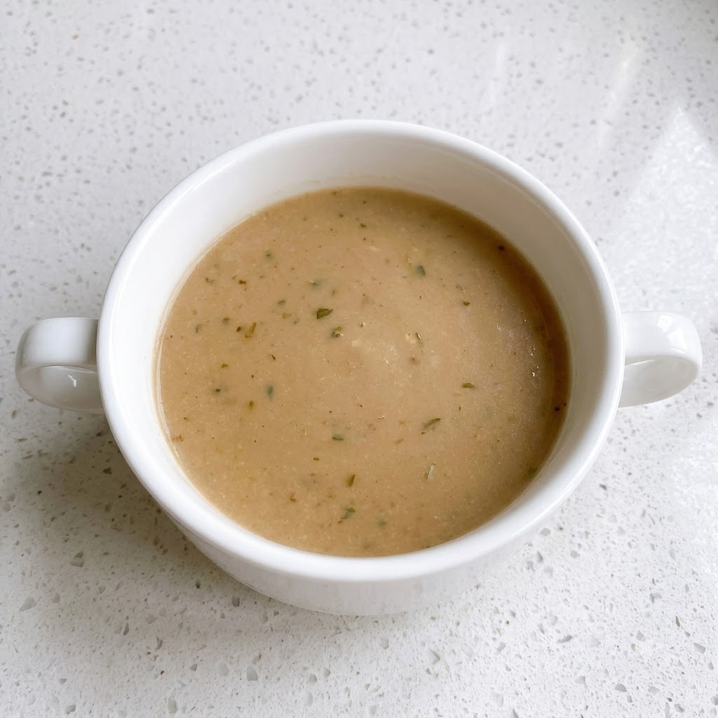 A white bowl containing a blended brown sauce mixture with pepper flecks.