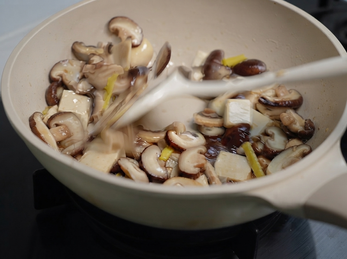 Mixed mushrooms and ginger being stir-fried in a pan with a spatula.