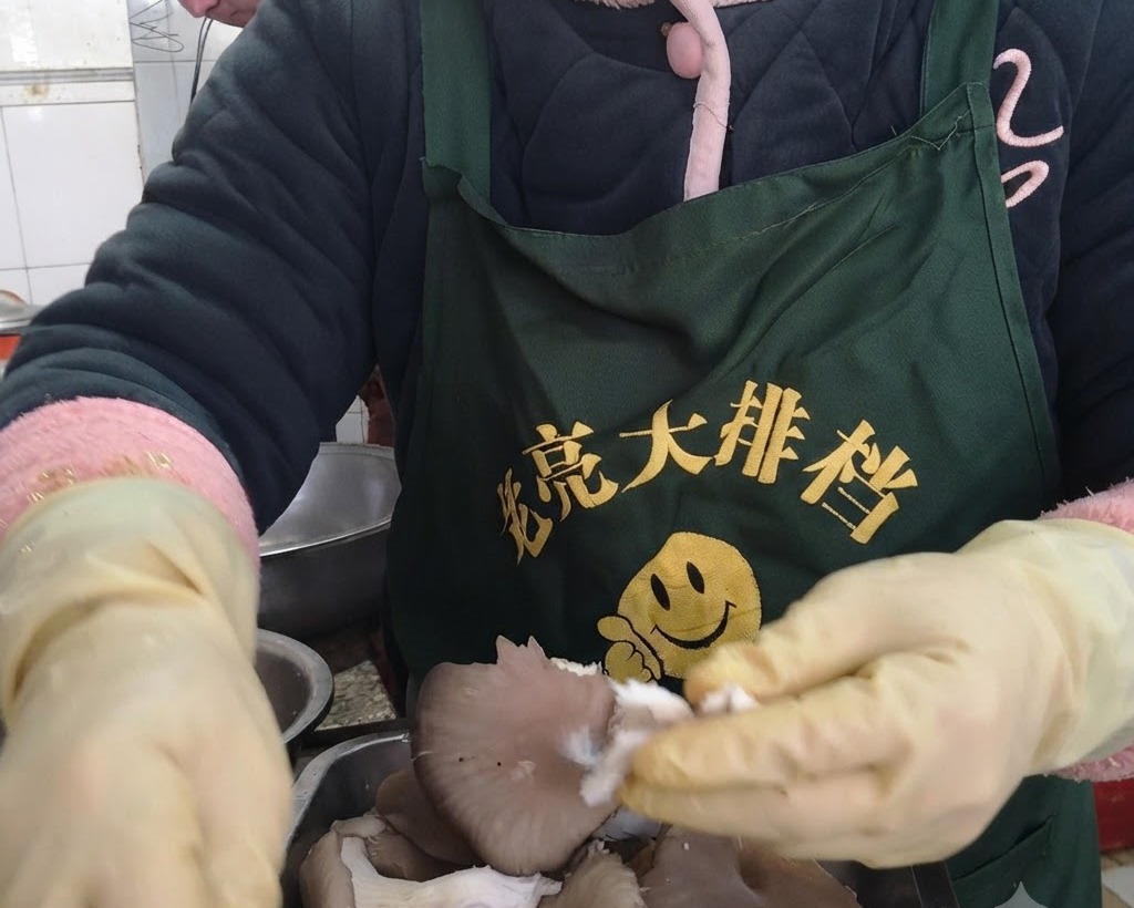 Hands wearing protective yellow gloves tearing fresh oyster mushrooms into individual strips.