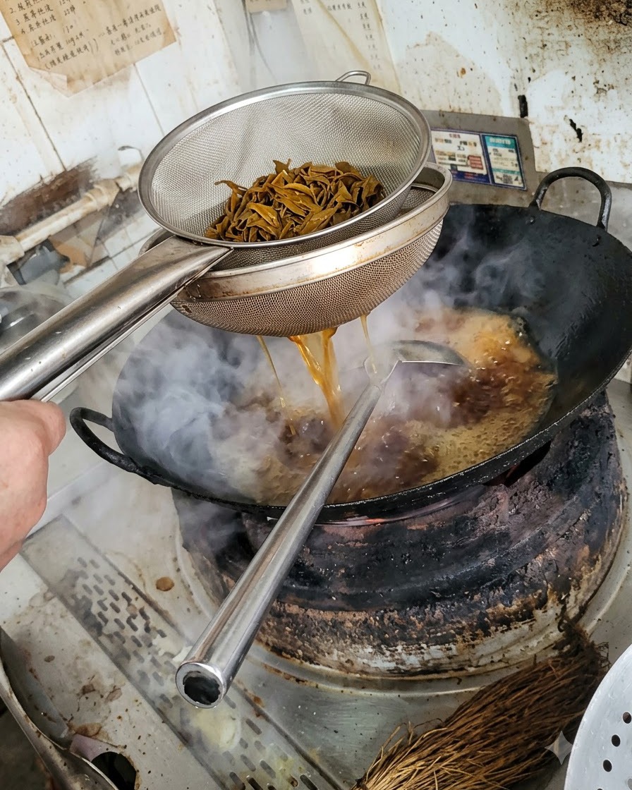 A metal colander holding dark blanched mushroom strips, with liquid draining back into the wok below.