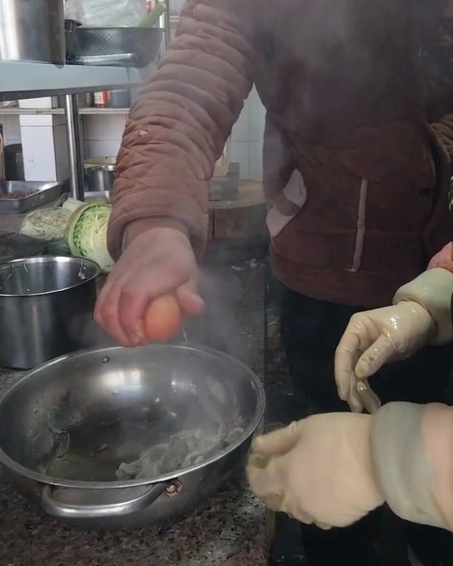 A person cracking a fresh brown egg into a stainless steel bowl containing the prepared mushrooms.