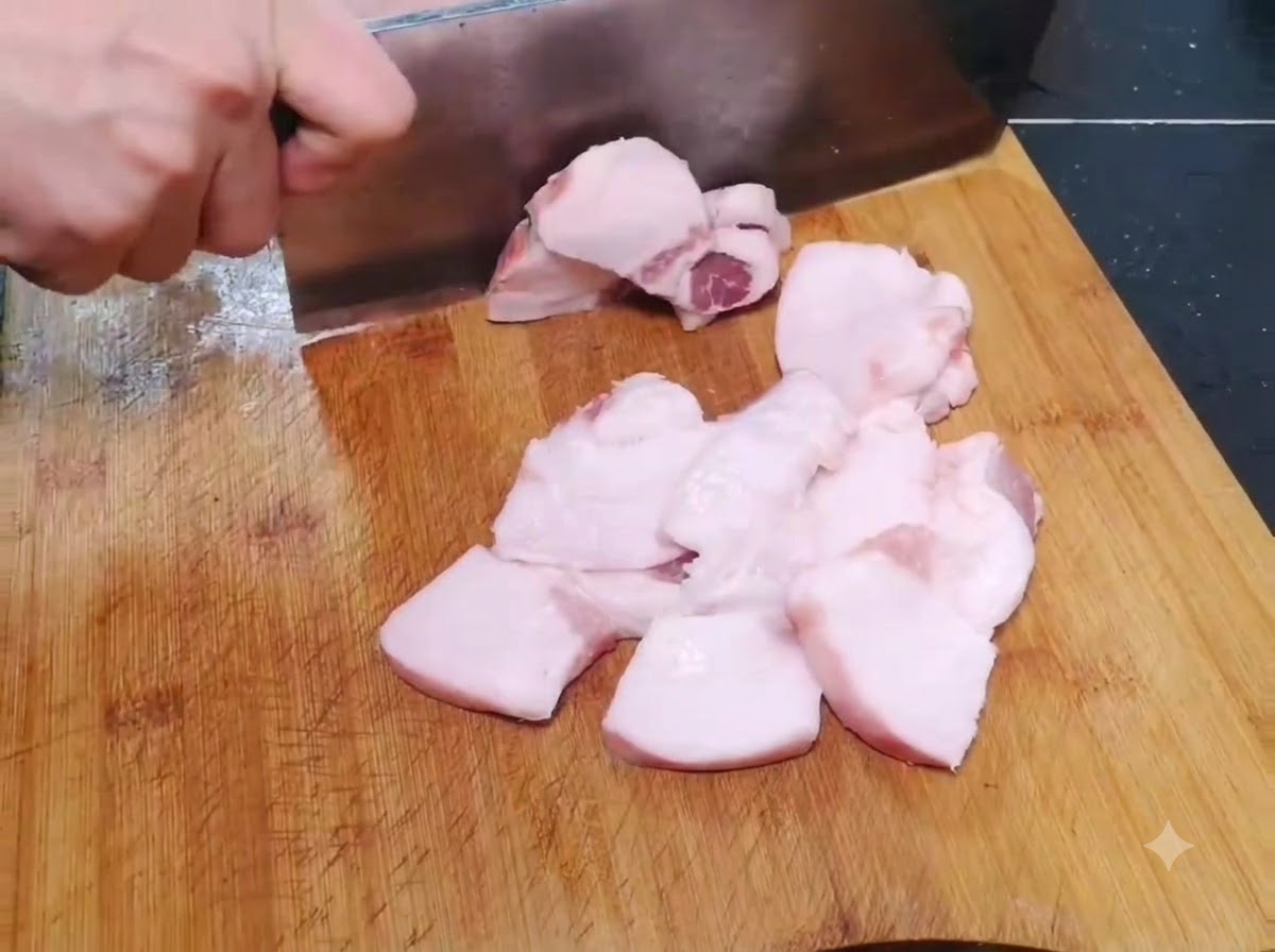Thin, wide pieces of raw pork being sliced on a wooden cutting board.