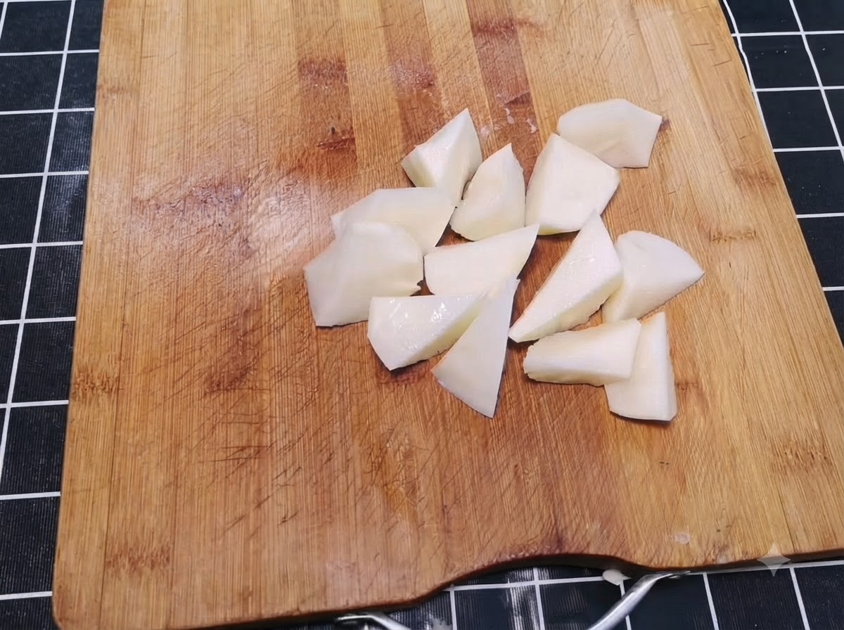Peeled potatoes cut into irregular bite-sized chunks scattered on a wooden cutting board.