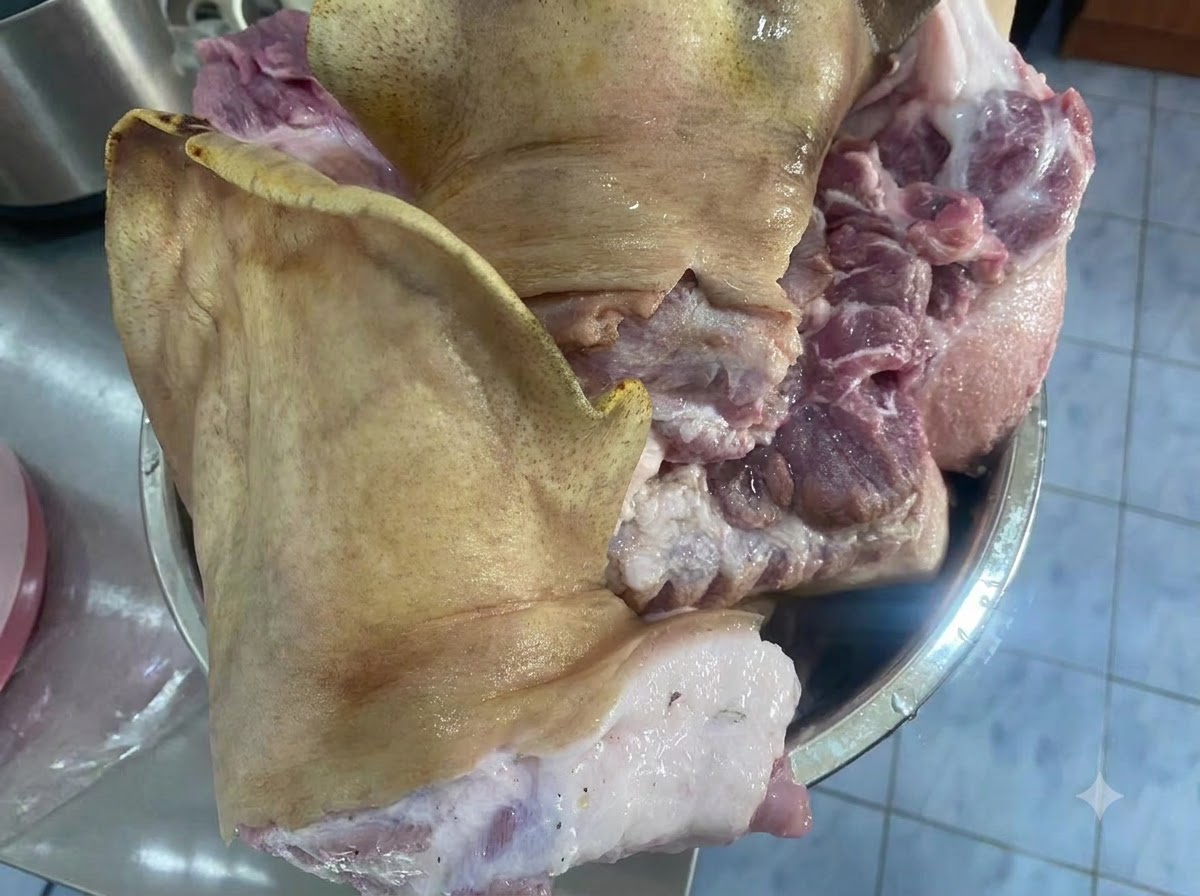Large raw pieces of a pig face resting inside a metal bowl on a countertop.