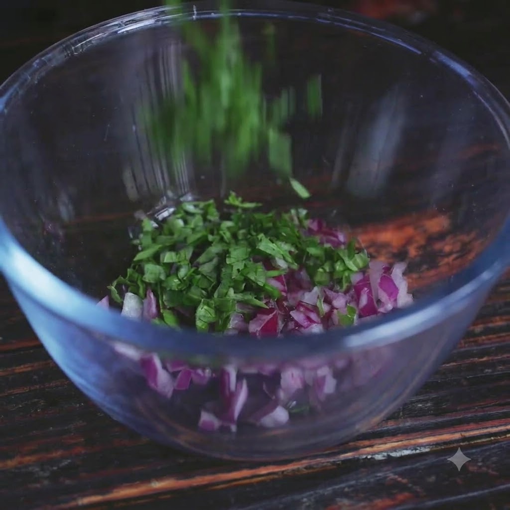 Fresh green herbs being dropped into a clear glass bowl containing chopped red onions.