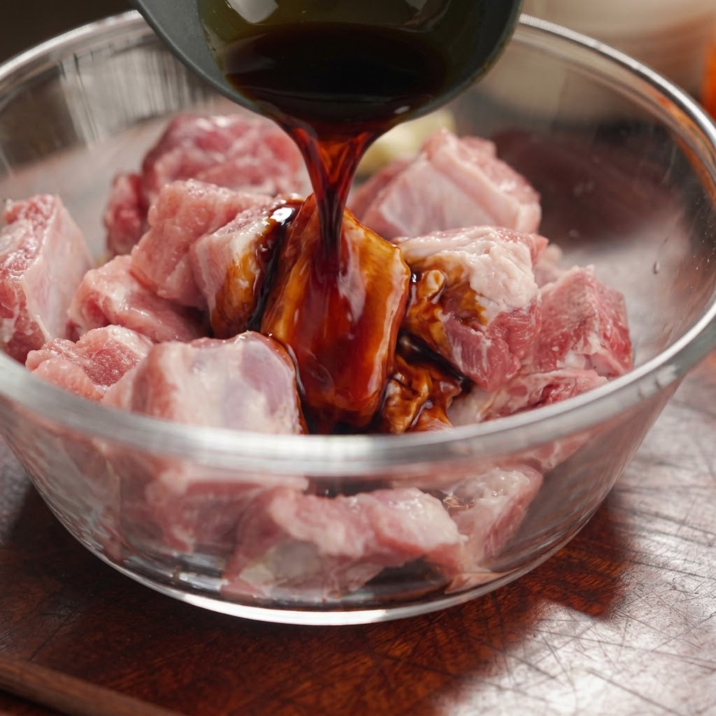 Dark soy sauce being poured from a ladle onto raw pork rib pieces in a glass bowl.