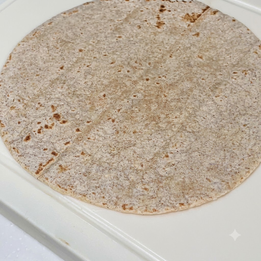 A whole wheat tortilla layered with peanut butter sauce, sliced chicken, purple cabbage, and fresh lettuce.