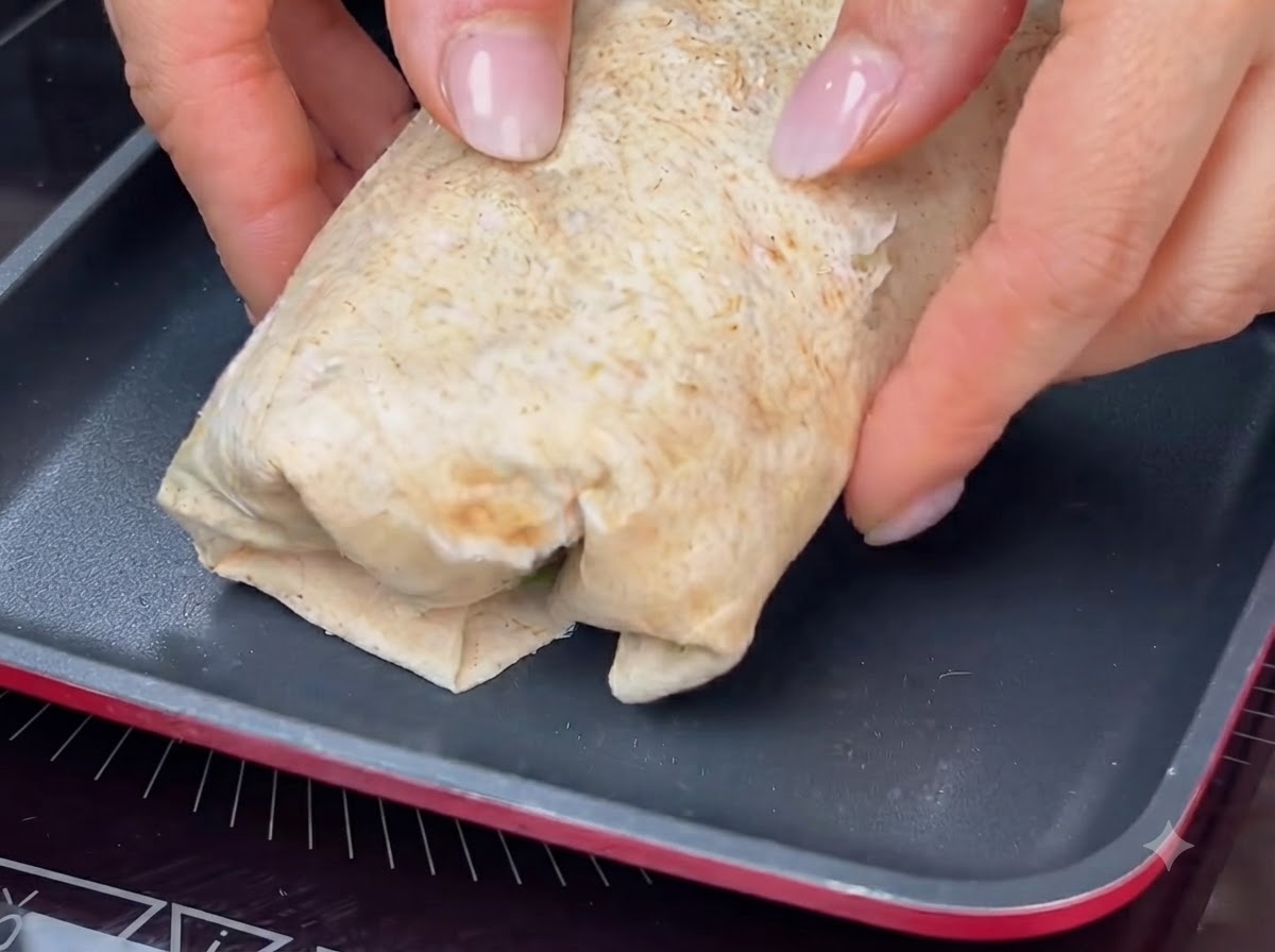 A rolled wrap being toasted in a hot pan to achieve a golden-brown crust.