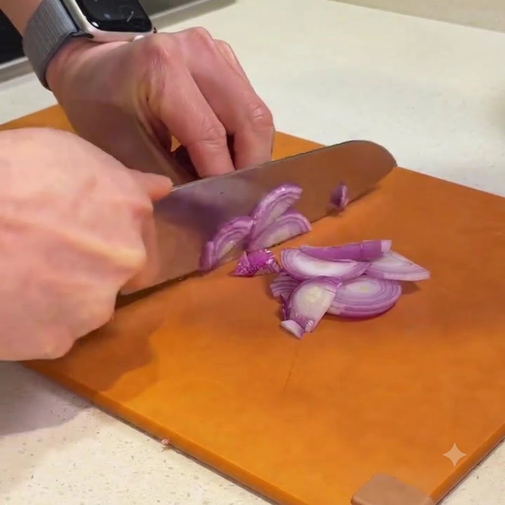 Red shallots being sliced and chopped into fine pieces on an orange cutting board.