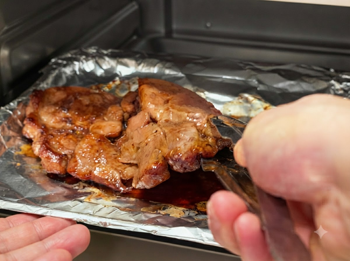 Pork chops being flipped over on the baking tray using metal kitchen tongs.