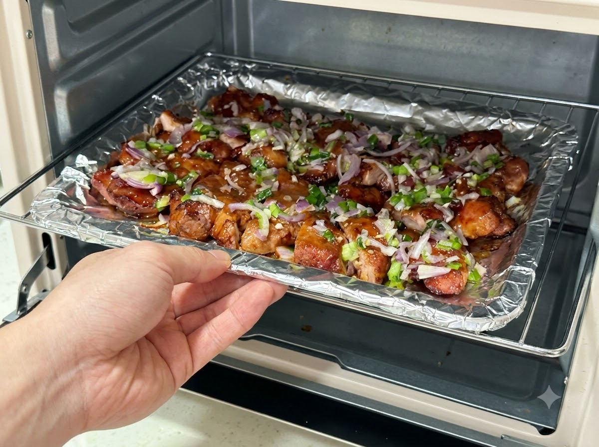 A baking tray loaded with sauce-covered pork slices being slid back into an air fryer.