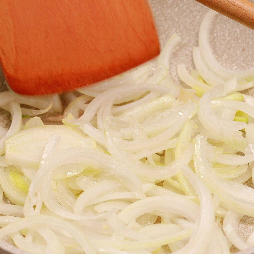 Shredded onions cooking in a pan being moved around by a wooden spatula.