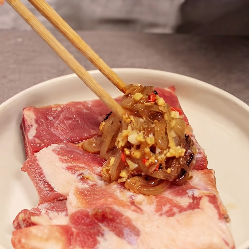 Chopsticks holding a portion of the onion and sauce mixture over raw pork ribs on a white plate.