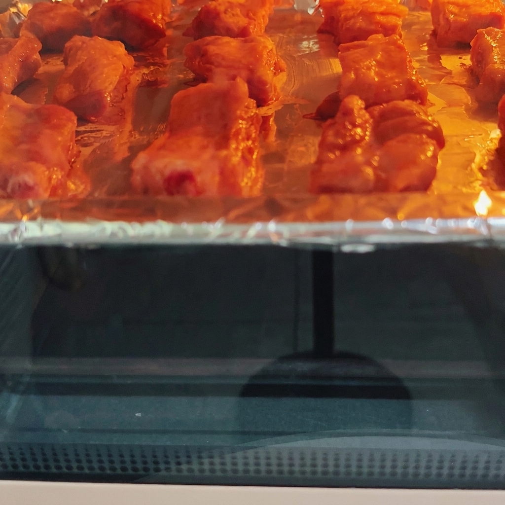 Pork ribs roasting inside a hot oven on a tray, showing visible browning under the heating element.