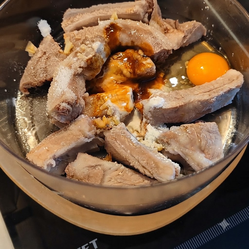 Pork ribs being marinated with various sauces and a cracked egg in a mixing bowl.