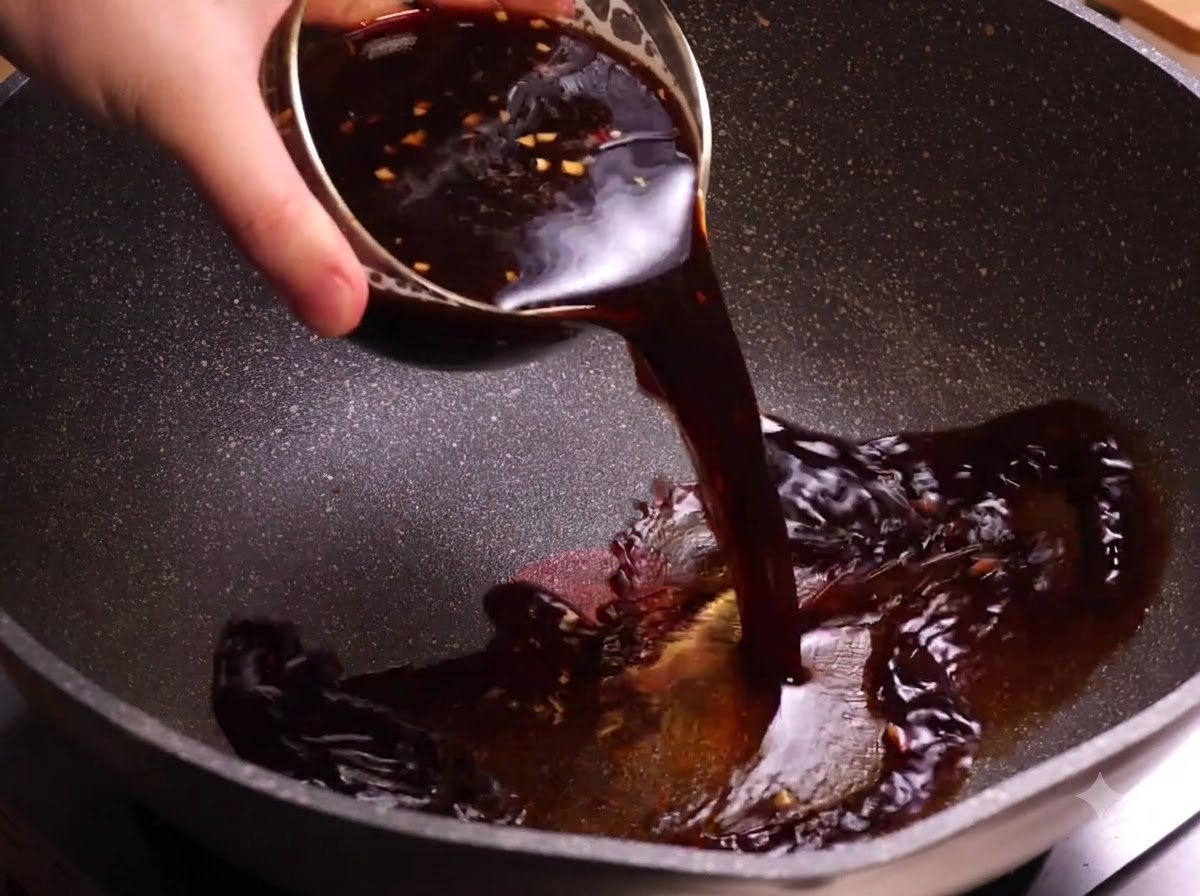 A bowl of dark coffee sauce being poured into a heated wok.